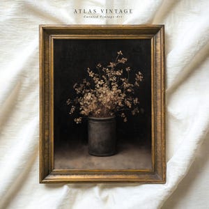 May include: Vintage framed artwork featuring a still life of dried flowers in a dark gray pot against a black background. The artwork is in a gold-colored ornate frame. The text "ATLAS VINTAGE Curated Vintage Art" is at the top.