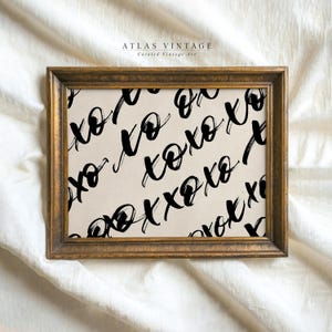May include: A framed art print with a gold-toned frame. The artwork features a cream-colored background with a repeating pattern of black "xo" script. The print is from Atlas Vintage, Curated Vintage Art.