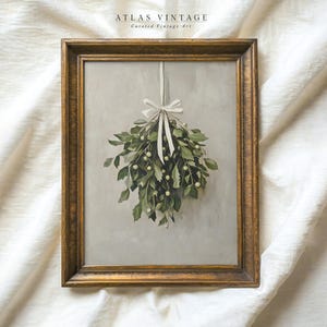 May include: A framed painting of a sprig of mistletoe with white ribbon hanging from a ceiling. The painting is in a gold frame and has a light gray background.