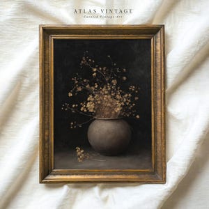 May include: Vintage framed artwork featuring a still life of dried flowers in a gray vase against a dark background. The artwork is in a gold-colored frame. The text "ATLAS VINTAGE Curated Vintage Art" is at the top.
