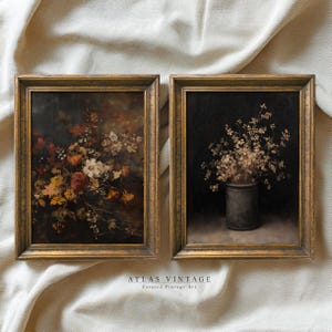 May include: Two framed vintage floral paintings. One features a dark background with colorful flowers, the other a vase of dried flowers against a black backdrop. Both are in gold-toned frames. The text "ATLAS VINTAGE" is visible.