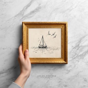 May include: A framed pen and ink drawing of a sailboat on the water with three birds in flight. The artwork is in a gold-colored frame. The text "ATLAS VINTAGE" and "Curated Vintage Art" is at the bottom of the frame.
