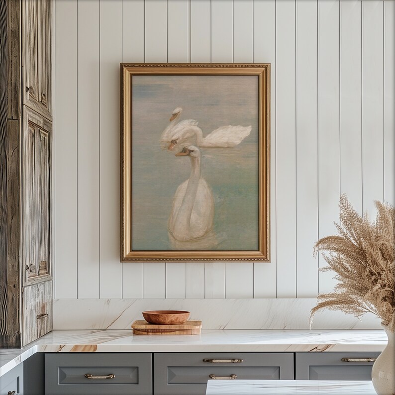 May include: A framed painting of two white swans swimming in a lake. The painting has a gold frame and a light blue background.
