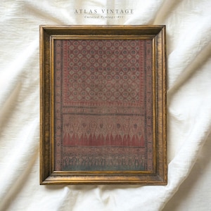 Könnte beinhalten: Gerahmtes Vintage-Textilkunstwerk in einem goldfarbenen Holzrahmen. Der Stoff zeigt ein rotes und graues Muster mit geometrischen und floralen Motiven. Oben auf dem Rahmen steht "ATLAS VINTAGE" und "Curated Vintage Art".