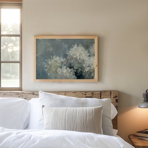 May include: A framed painting of white hydrangeas with a blue and green background. The painting is hanging on a wall above a white bed with a wooden headboard.