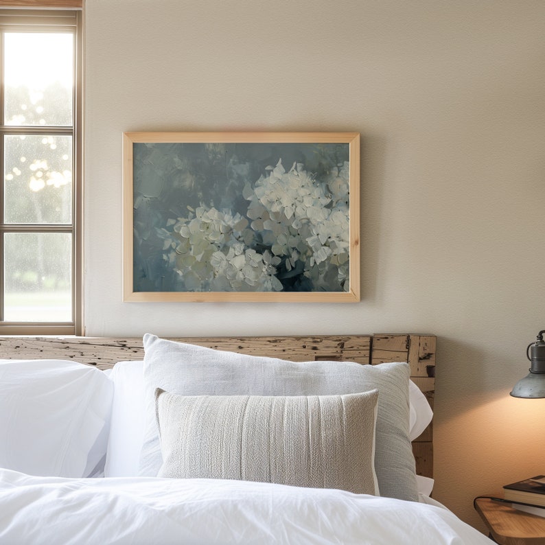 May include: A framed painting of white hydrangeas with a blue and green background. The painting is hanging on a wall above a white bed with a wooden headboard.