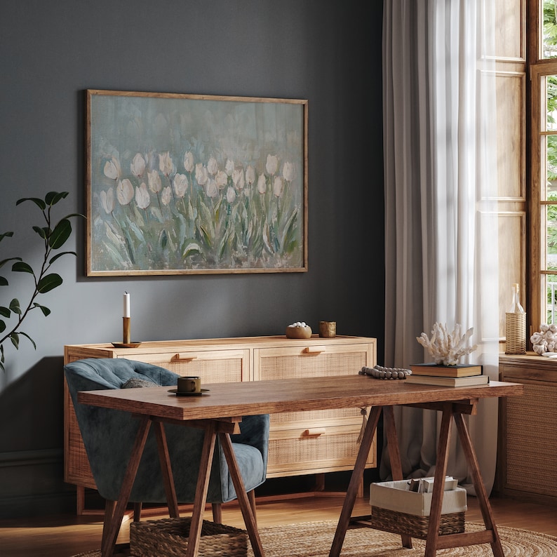 May include: A home office with a wooden desk and a blue chair. A large framed painting of white tulips hangs above a wooden cabinet. The room is decorated with a candle, books, and decorative coral.