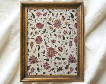 May include: A framed vintage print with a floral pattern in shades of pink, red, and green on a white background. The frame is gold and has a simple design.