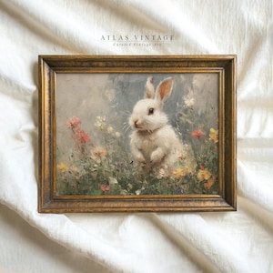 Puede incluir: Una pintura vintage enmarcada de un conejo blanco sentado en un campo de flores. El conejo mira hacia la izquierda y tiene un pelaje suave y esponjoso. Las flores son de color rosa, morado y amarillo. La pintura está enmarcada en un marco dorado.