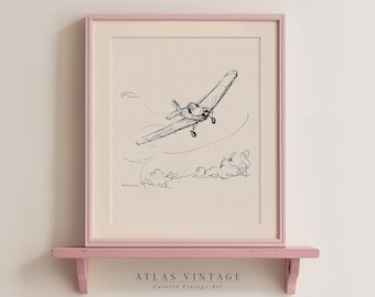 Pode incluir: Um desenho a preto e branco de um avião vintage a voar através das nuvens. O desenho está emoldurado numa moldura rosa claro e apresentado numa prateleira rosa claro.