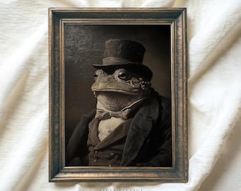 Pode incluir: Impressão vintage emoldurada em tons sépia, apresentando um elegante sapo em traje formal. O sapo usa cartola, terno e gravata borboleta. A moldura é de madeira escura. O texto "ATLAS VINTAGE" é visível na parte inferior.