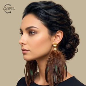 May include: Dangle earrings featuring brown and green spotted feathers suspended from a small gold-toned circular stud. The feathers have a layered, textured appearance with iridescent green accents. The text MY FEATHER EARRINGS is visible.
