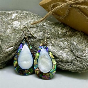May include: A pair of teardrop-shaped earrings with iridescent mother-of-pearl inlays. The earrings are made of silver and have a teardrop shape. The inlays are a mix of blue, green, and purple.