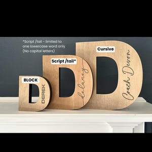 May include: Three wooden letters, each in a different style: block, script, and cursive. The letters are all the letter "D" and are personalized with names. The block letter says "Derek", the script letter says "Delaney", and the cursive letter says "Coach Devon".