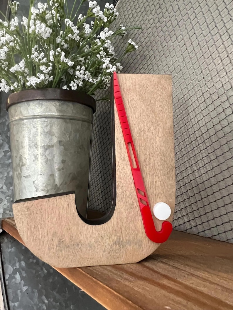May include: Wooden letter J with a red hockey stick and white puck. The letter is painted in a light brown color with a distressed finish.