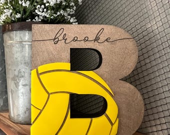 May include: A wooden letter B with a yellow volleyball design and the name "brooke" written in cursive on the top.