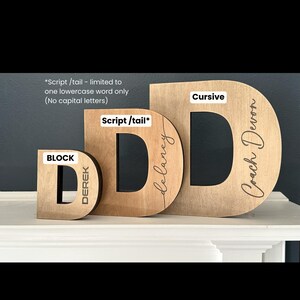 Pu&ograve; includere: Tre lettere in legno, ciascuna in uno stile diverso: blocco, scrittura e corsivo. Le lettere sono tutte la lettera "D" e sono personalizzate con nomi. La lettera in blocco dice "Derek", la lettera in scrittura dice "Delaney" e la lettera in corsivo dice "Coach Devon".