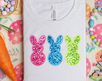 May include: White t-shirt with three glitter Easter bunny silhouettes. The bunnies are pink, blue, and green.
