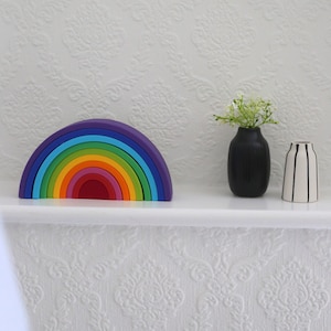 May include: A colourful wooden rainbow stacker toy in shades of purple, blue, green, yellow, orange, and red. A black vase with white flowers and a black and white striped vase are also on the shelf.