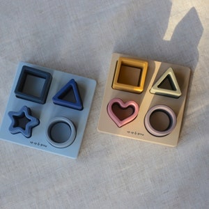 May include: Two wooden puzzle boards with different coloured shapes. The top board has a yellow square, green triangle, pink heart, and purple circle. The bottom board has a blue square, blue triangle, blue star, and blue circle. Both boards have the text "up & grow" on them.