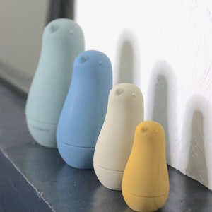 May include: Four bird-shaped ornaments in a row, in pastel shades of light blue, blue, cream, and yellow. Each has a rounded base and a small head with a beak detail. They are displayed on a dark surface.