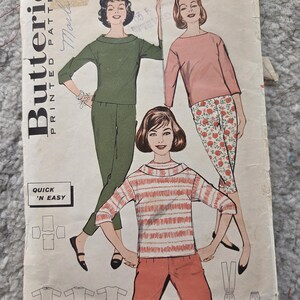 May include: Vintage Butterick printed patterns envelope. The cover shows illustrations of women in different outfits, including a green trouser suit, a pink top with floral trousers, and a striped top with orange trousers. The text "QUICK 'N EASY" is visible.