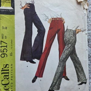 Op de afbeelding: Vintage McCall's 9517 Misses' broekenset naaipatroon. Het patroon toont illustraties van drie verschillende flared broeken in marine, rood en een patroonstof. Het patroon bevat de tekst "New Sizing".