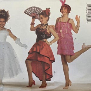 Puede incluir: Un sobre de patrón Butterick vintage con tres diseños de disfraces. Uno es un vestido de tul blanco con detalles brillantes, otro es un vestido rojo y negro de estilo flamenco, y el tercero es un vestido de flapper rosa. El sobre incluye el texto "NEW YORK FABRICS".