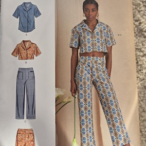 May include: Simplicity sewing pattern U5, featuring a short-sleeved shirt, cropped top, pants, and shorts. The pattern includes sizes 16-24. The image shows a woman wearing a matching top and pants set with a blue, orange, and white geometric pattern.