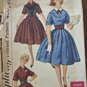 May include: Vintage Simplicity sewing pattern featuring illustrations of dresses. The dresses include a red plaid dress with a black bodice, and a blue dress with a floral pattern. The pattern is marked with the number 3594 and the words "Simple to make".