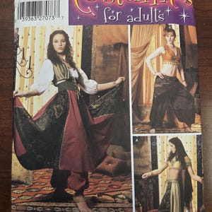 Puede incluir: Un patrón Simplicity para disfraces de adultos. La portada presenta a tres mujeres con diferentes diseños de disfraces, incluyendo una falda larga y top, y pantalones harén. El patrón incluye tallas 6, 8, 10 y 12.