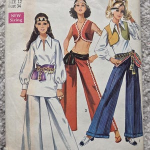 Peut inclure: Un patron de couture Simplicity vintage présentant trois tenues des années 1970. Le patron comprend un tailleur pantalon blanc, un ensemble crop top et pantalon rouge, et un tailleur pantalon rayé bleu avec un gilet. Le patron est pour la taille Misses 12, tour de poitrine 86 cm.