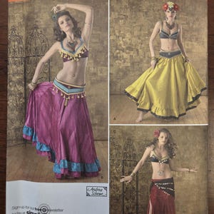 Puede incluir: Patrón de costura Simplicity 2158 con tres diseños de disfraces de danza del vientre. El patrón incluye imágenes de los disfraces, con una variedad de estilos de faldas y tops. El tamaño del patrón es HH 6,8,10,12, EUR 32-38, FR 34-40.