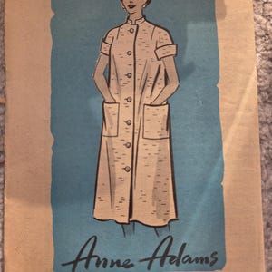May include: Vintage sewing pattern featuring an illustration of a woman in a button-down dress with pockets. The pattern is labeled "Anne Adams 4530-SIZE 16" on a blue background. The overall color scheme is beige and blue.