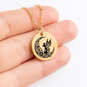 May include: Gold necklace with a round pendant featuring a black silhouette of a fairy sitting on a crescent moon with floral details.