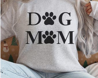 May include: A light gray sweatshirt with the words "DOG MOM" in black block letters, with paw print graphics replacing the "O" letters. The sweatshirt is made of a soft material.