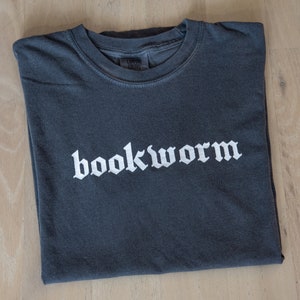 Op de afbeelding: Een donkergrijs T-shirt met het woord "bookworm" in witte gotische letters.
