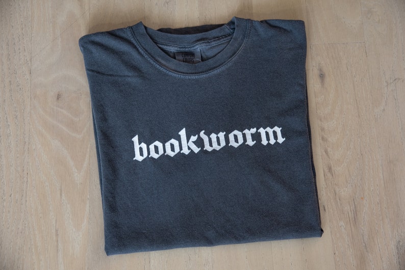 Op de afbeelding: Een donkergrijs T-shirt met het woord "bookworm" in witte gotische letters.