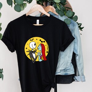 Pu&ograve; includere: Maglietta nera con una grafica di Jack Skellington e Sally di The Nightmare Before Christmas. La grafica li mostra mano nella mano davanti a una luna gialla con pipistrelli che volano intorno.