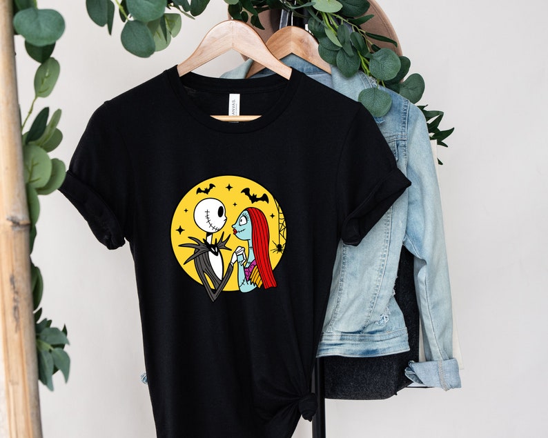 Pu&ograve; includere: Maglietta nera con una grafica di Jack Skellington e Sally di The Nightmare Before Christmas. La grafica li mostra mano nella mano davanti a una luna gialla con pipistrelli che volano intorno.