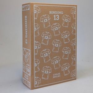 May include: A hardcover book titled "Binding 13" by Chloe Walsh. The cover is tan with a repeating pattern of white t-shirts with the number 13. The spine also features the title and author's name.