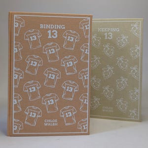 May include: Two hardcover books. The first, "Binding 13," is tan with white jersey graphics and the text "13." The second, "Keeping 13," is light green with white strawberry graphics. Both books have the author's name.