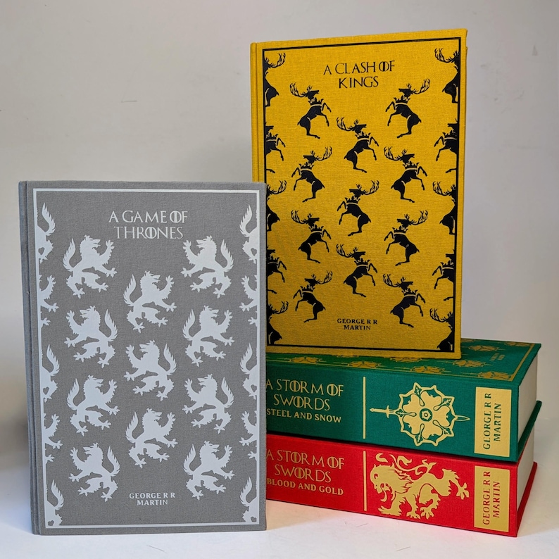 May include: A collection of hardcover books featuring the "Game of Thrones" series. The books have decorative covers in various colors, including gray, yellow, green, and red. The titles and author's name are printed on the spines and covers.