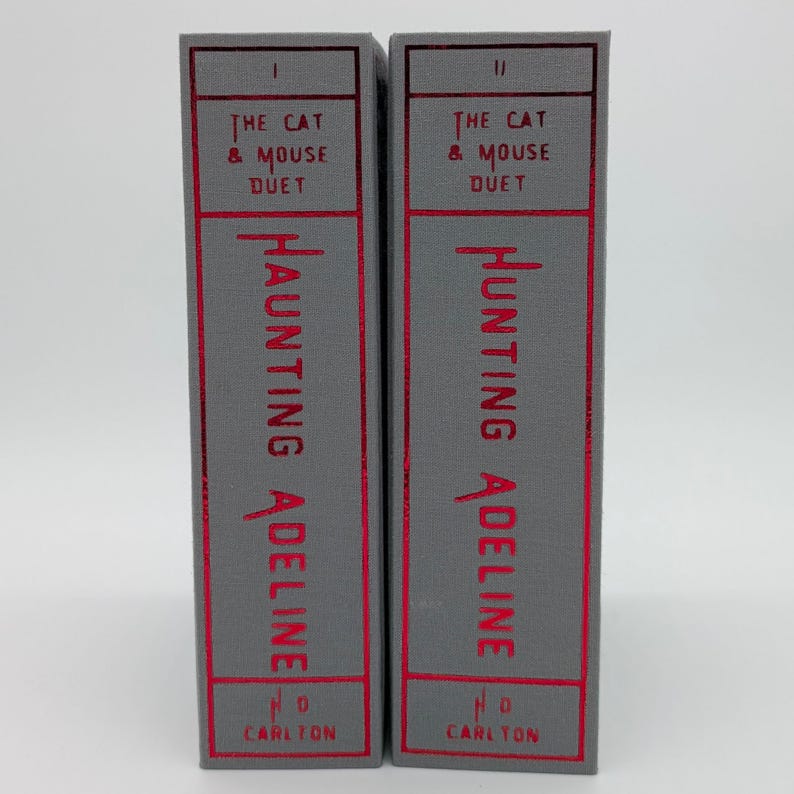May include: Two hardcover books, "The Cat & Mouse Duet" series, are displayed. The spines are gray with red text that reads "Haunting Adeline" and "Hunting Adeline". The publisher's name, "H.D. Carlton", is at the bottom.
