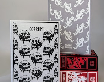 May include: A stack of books with unique cover designs. The book titled "Corrupt" features a pattern of black skulls on a silver background. The book "Hideaway" has a gray cover with a repeating white design. The spines of the books below are red and black.