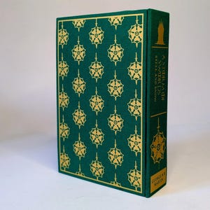 May include: A hardcover book with a green cover featuring a repeating gold floral pattern. The spine displays the title "A Storm of Swords" and the author's name, George R.R. Martin. The book's design is detailed and decorative.