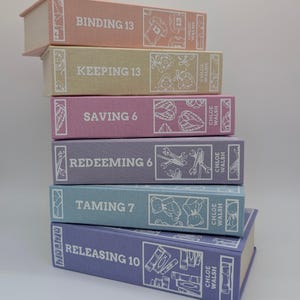 Könnte beinhalten: Ein Stapel aus sechs gebundenen Büchern mit pastellfarbenen Stoffeinbänden. Die Buchrücken zeigen weißen Text, darunter die Titel Binding 13, Keeping 13, Saving 6, Redeeming 6, Taming 7, Releasing 10 und den Namen Chloe Walsh mit grafischen Motiven.