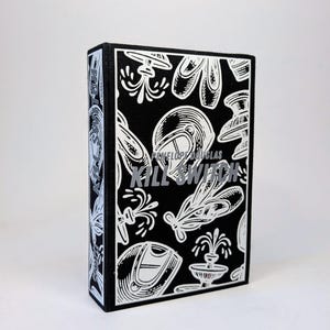 Puede incluir: Una caja negra con un patrón blanco de varios objetos, incluyendo un casco, zapatos y una fuente. El texto "PENELOPE DOUGLAS" y "KILL SWITCH" está impreso en la parte frontal de la caja.