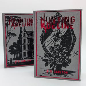 May include: Two hardcover books with the title "Hunting Adeline" in red foil lettering. One book features a haunted house illustration, the other a broken mirror with roses. Both have red borders and the author's name.