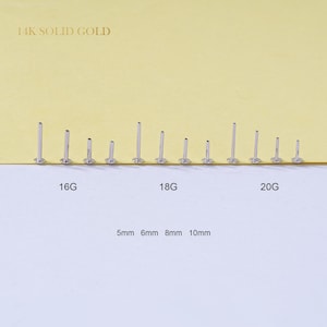 May include: A collection of silver-colored, straight-post earrings in varying lengths, displayed on a white surface. The earrings are labeled with sizes 16G, 18G, and 20G, and lengths of 5mm, 6mm, 8mm, and 10mm. The text "14K SOLID GOLD" is at the top.